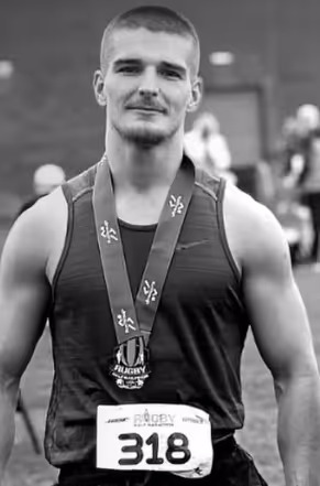 Damien Goring Personal Trainer in a black and white photo wearing a badge with number "318" having completed a running event.
